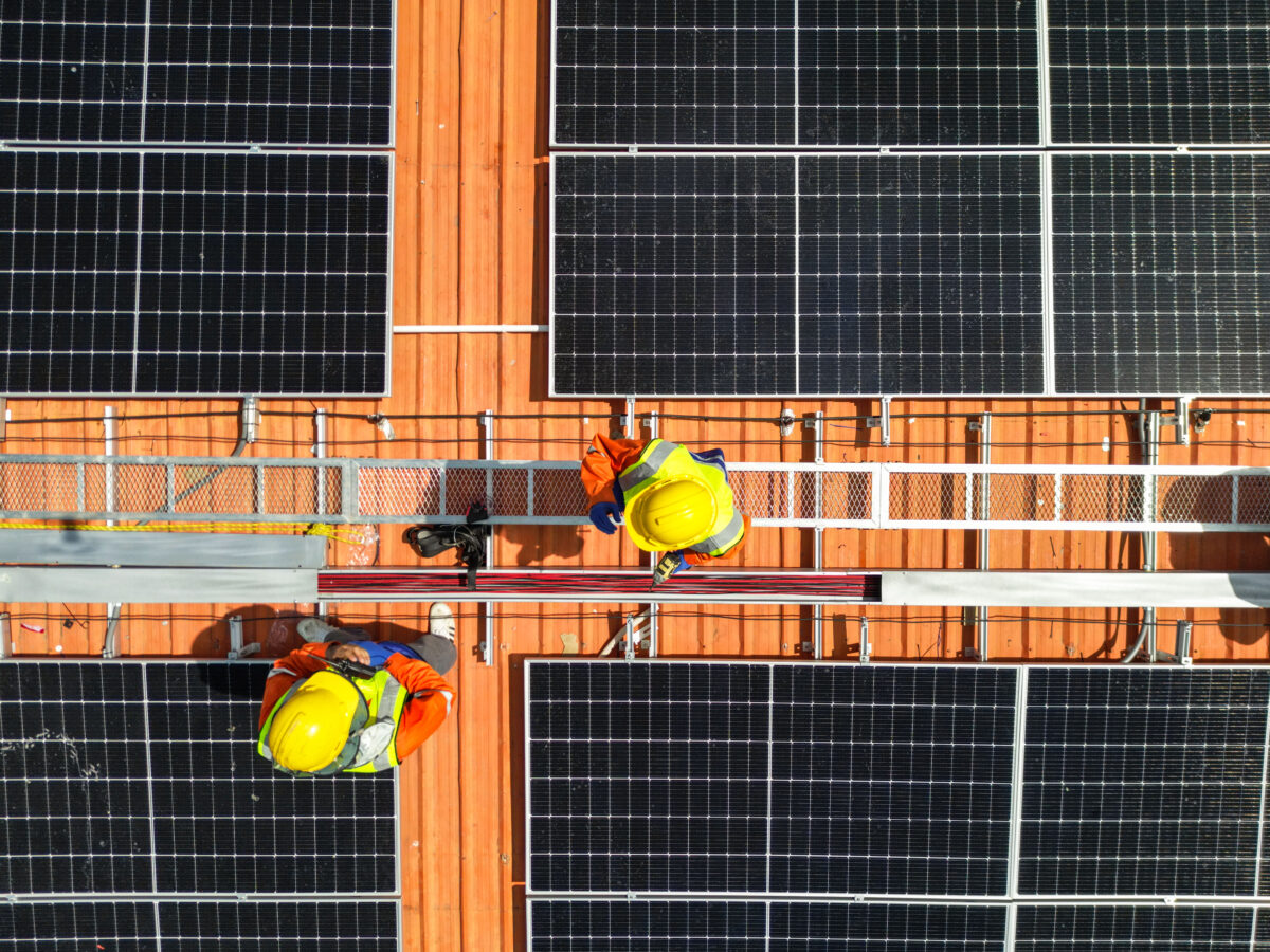 top aerial of engineer men inspects construction of solar cell panel or photovoltaic cell at roof top. Industrial Renewable energy of green power. factory at urban area. worker working on tower roof.