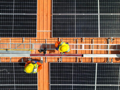 top aerial of engineer men inspects construction of solar cell panel or photovoltaic cell at roof top. Industrial Renewable energy of green power. factory at urban area. worker working on tower roof.