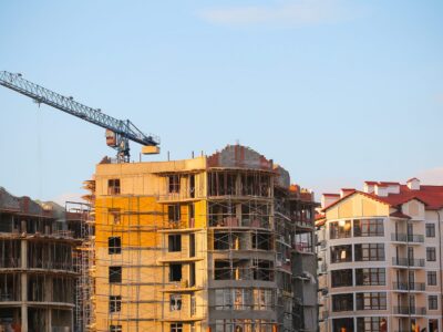Multifamily housing under construction with a tower crane, alongside a completed apartment building.